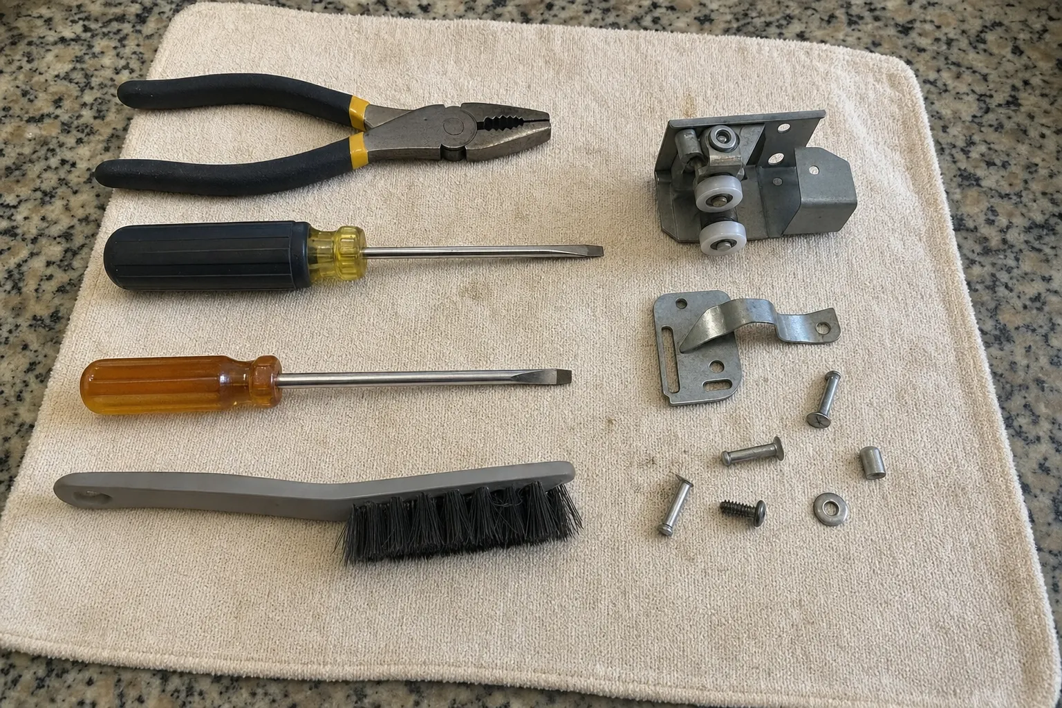 Lineman pliers, two flat screwdrivers and a brush beside a steel bracket carrying two white rollers, a bent clip plate and loose rivets